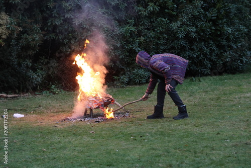 A person is standing over a fire, holding a stick