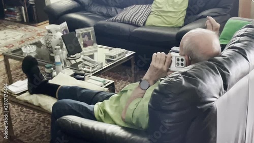 Abuelo usando smartphone viejo con teléfono hablando en salón anciano sentado hablando por el móvil y gesticulando con la mano tercera edad y celular en sofá vídeo doméstico gestual expresivo