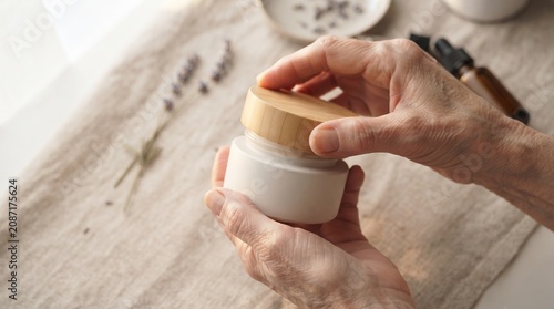 Elderly person hands holding a white cream jar with wooden lid
