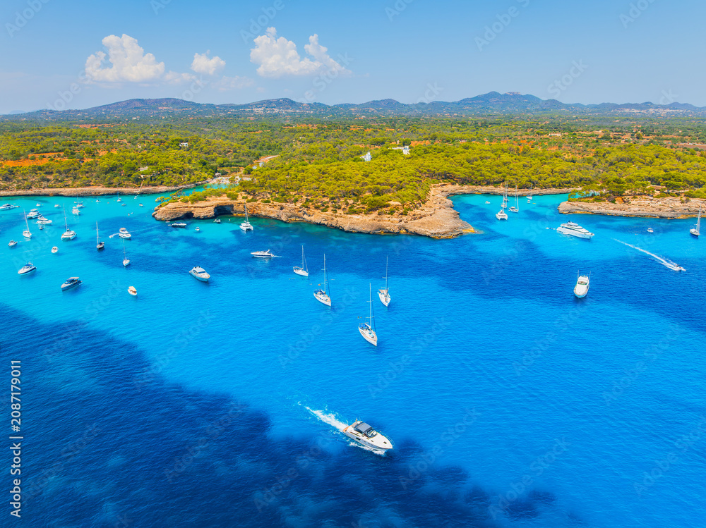 Obraz premium Aerial drone view of yachts and boats in a sea bay in Mallorca, Spain. Summer vacation, leisure and recreation near the Mediterranean coastal forest.