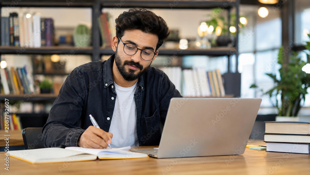 Fototapeta premium Bearded student working on laptop in bright workspace