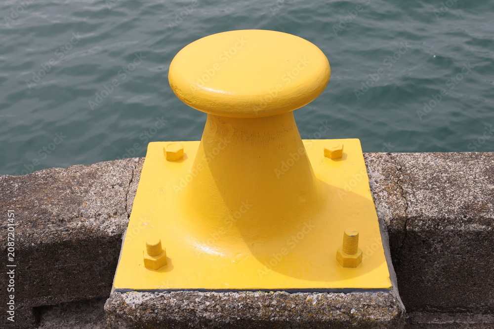 Obraz premium yellow maritime mooring bollard, cast iron or cast steel, anchored directly into concrete quay (close-up, waterfront) 4657