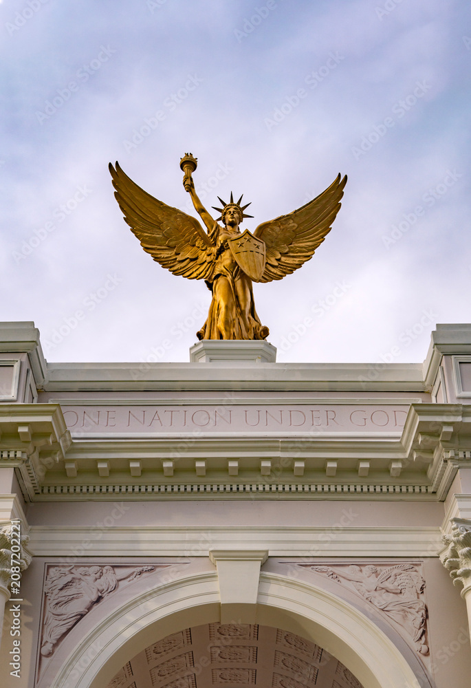 Obraz premium Golden statue crowns ceremonial arch. One nation under God. Patriotic golden statue above columns. Historic golden statue honors liberty. Golden statue stands over gateway.