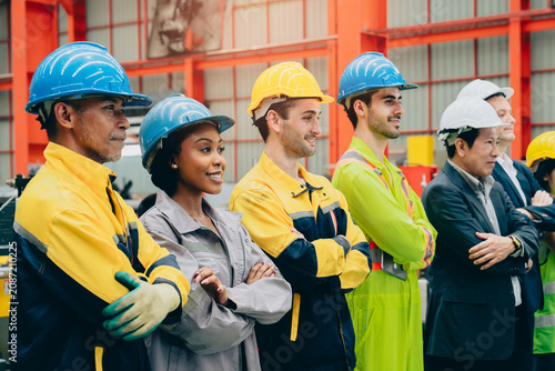 Industrial worker team in hard hat standing together with crossed arm inside factory