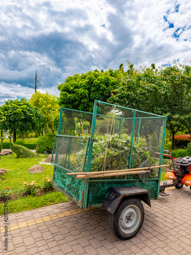 Garden trailer parked on a sunny day. A garden trailer filled with plants is parked beside a green area with trees and blue sky.