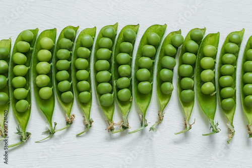 Close-up of ripe green peas inside opened pods in a row displayed on a bright white background, emphasizing healthy eating and seasonal vegetable harvest.