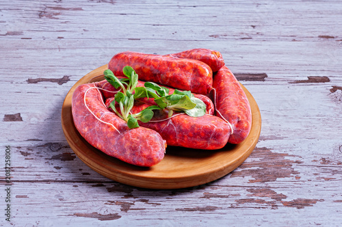 Billede på lærred Fresh raw chorizo sausages on wooden plate with green salad leaves on rustic bac