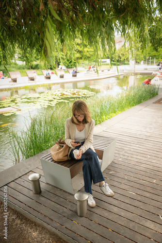 Mature business woman checking her smartphone during a coffee break in a city park