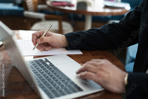Businessman writing notes while working on laptop