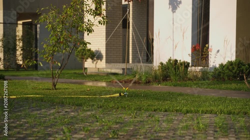 Automatic sprinkler system watering green grass and plants in a backyard, with a contemporary house providing a serene and scenic background for the garden scene