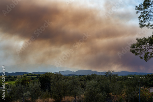 Billede på lærred Pyrénées-Orientales, France, July 5, 2026: Smoke from the Trévillach wildfire spreads over Mediterranean hills and wooded vegetation near Perpignan during a major wildfire in southern France