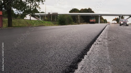 Road construction work with hot asphalt paving on a new highway lane with cars passing in the background