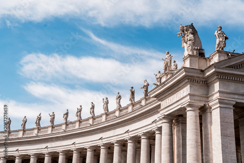 Curving colonnade with stone columns and a row of classical statues along the entablature at St. Peter's Square, Vatican City, Rome