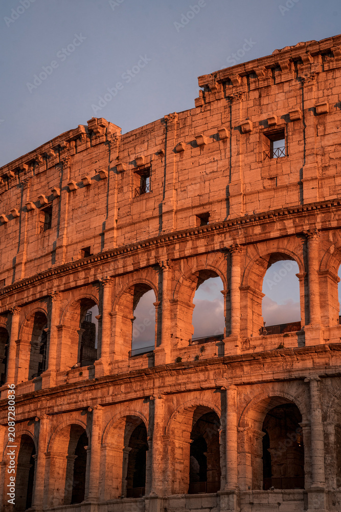 Obraz premium Ancient Colosseum exterior in Rome at golden hour, sunlit stone arches and weathered facade of amphitheater