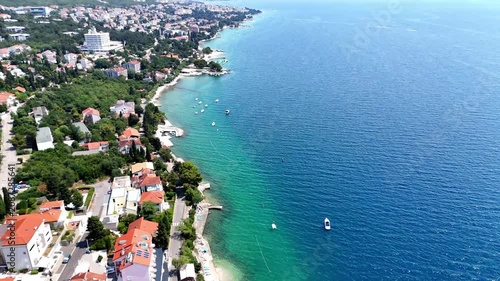 Top-down aerial drone shot of a modern city embankment promenade next to calm turquoise water with reflections.