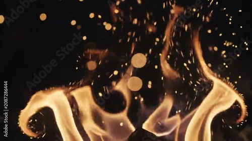 Closeup of bright orange flames and glowing embers rising against a dark black background