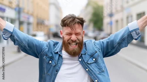 Portrait of overjoyed bearded man standing with excited expression, raising fists, screaming, shouting yeah, celebrating his victory, success.