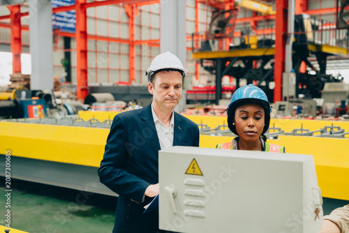 Industrial worker and manager inspect control panel in factory with hard hat and safety gear