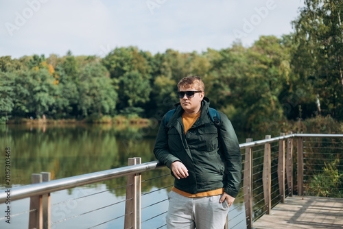A guy standing on a pier, a man meeting the dawn of the day in the morning on the lake, a hipster in a sunglasses wearing stylish outfit relaxing