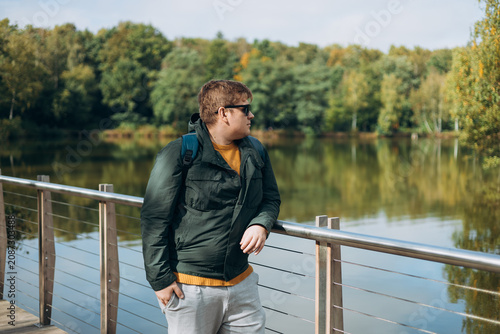 A guy standing on a pier, a man meeting the dawn of the day in the morning on the lake, a hipster in a sunglasses wearing stylish outfit relaxing