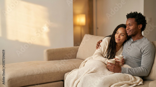 African American couple watching movie at home - Couple relaxing together on sofa with warm drinks and blanket  