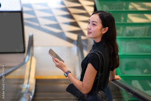 An attractive Asian woman looks back while riding an escalator inside a modern shopping center.