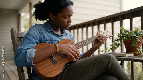 African American girl playing ukulele - Young black girl playing ukulele while sitting on porch  
