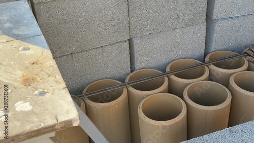 Stacked concrete blocks and cylindrical pipes in construction zone. Neat rows show building materials ready for use. Image captures industrial site with raw textures and practical setup