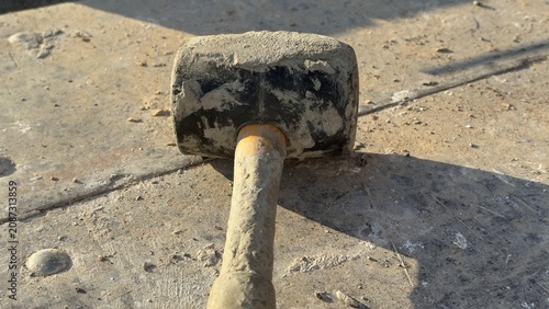 Worn rubber mallet rests on dusty concrete ground. Tool shows signs of heavy use. Ideal for construction, DIY, or repair themed content. Suggests manual labor or home improvement projects