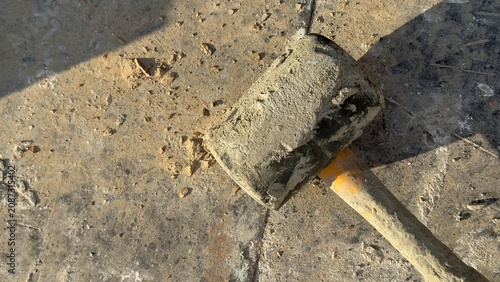 Worn rubber mallet rests on dusty concrete ground. Tool shows signs of heavy use. Ideal for construction, DIY, or repair themed content. Suggests manual labor or home improvement projects