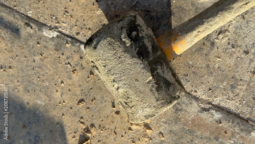 Worn rubber mallet rests on dusty concrete ground. Tool shows signs of heavy use. Ideal for construction, DIY, or repair themed content. Suggests manual labor or home improvement projects