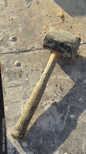 Worn rubber mallet rests on dusty concrete ground. Tool shows signs of heavy use. Ideal for construction, DIY, or repair themed content. Suggests manual labor or home improvement projects