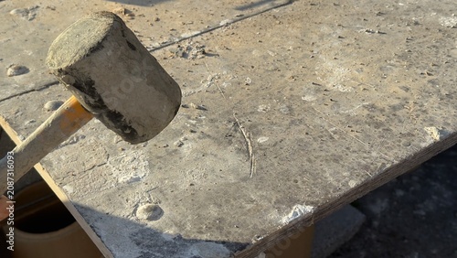Worn rubber mallet rests on dusty concrete ground. Tool shows signs of heavy use. Ideal for construction, DIY, or repair themed content. Suggests manual labor or home improvement projects