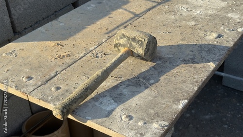 Worn rubber mallet rests on dusty concrete ground. Tool shows signs of heavy use. Ideal for construction, DIY, or repair themed content. Suggests manual labor or home improvement projects