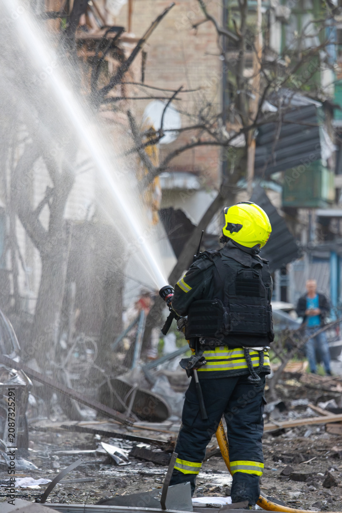 Fototapeta premium Brave firefighter battling a blaze amidst debris and a burnt car wreckage