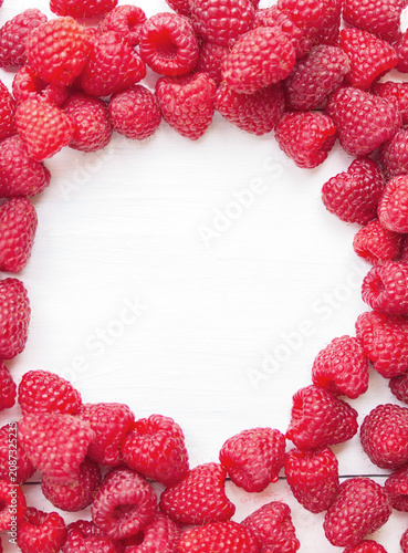 A top view frame of fresh red raspberries arranged on a white wooden background with empty copy space.