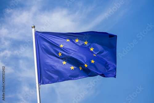 Flag of the European Union waving in the wind on flagpole against the sky with clouds on sunny day, close-up