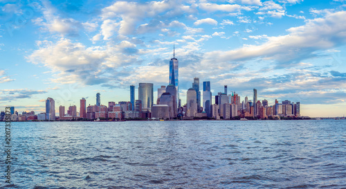 Wide-angle panoramic view of the iconic New York City skyline in the early evening, captured from the waterfront in Jersey City, New Jersey, across the Hudson River.