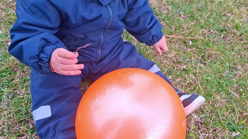 Toddler in blue jumpsuit playing with orange balloon