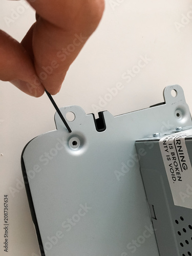 Hand unscrewing a screw on the metal casing of a car radio with a screwdriver.