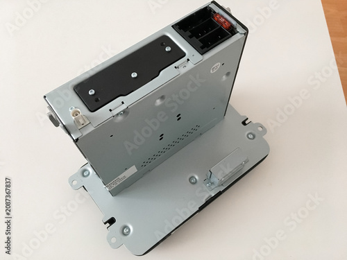 Car radio unit standing on a white table showing its metal mounting bracket and casing.