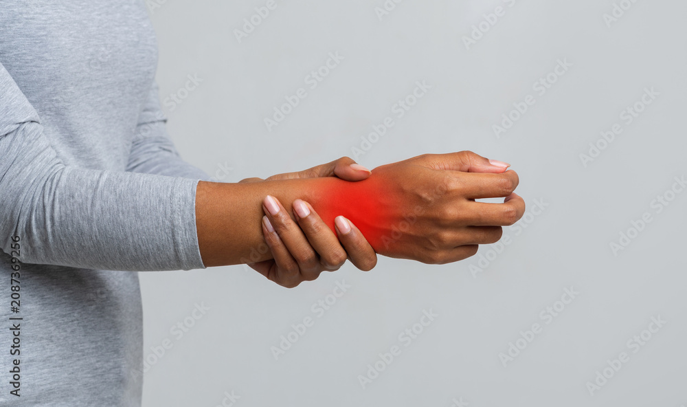 Fototapeta premium Cropped image of African American woman suffering from rheumatism, massaging her wrist, grey background