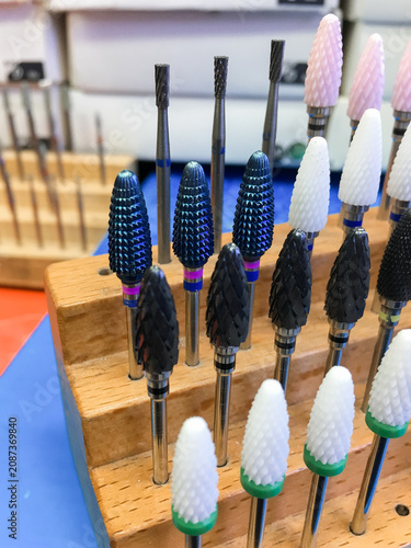 Set of nail drill bits standing on a wooden holder on a blue mat.