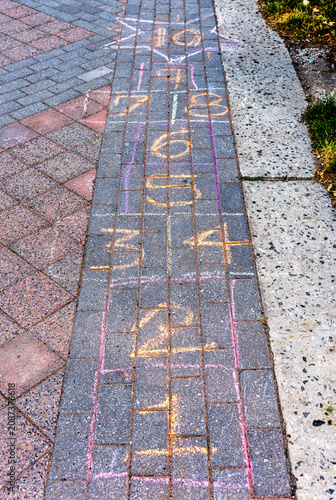 A top-down shot reveals colourful, hand-drawn chalk hopscotch squares sketched across a weathered brick pavement, capturing a nostalgic slice of urban childhood play.