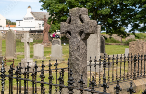 A close, selective-focus view of an ornate memorial cross in a churchyard, highlighting its intricate carvings while the surrounding grounds fade softly into the background.