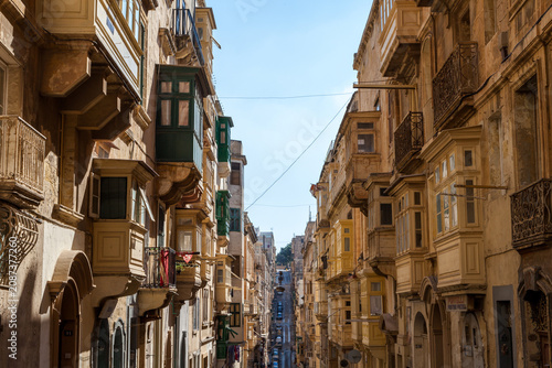 Картината върху платно A narrow street in Valletta, Malta, lined with traditional limestone buildings f