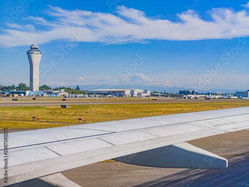 Airplane wing view of airport control tower and Mount Rainier