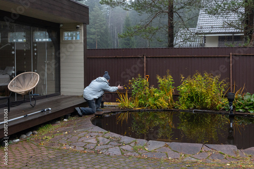 Bild auf Leinwand Removing debris from small pond using hands man caring for garden water feature autumn cleanup scene