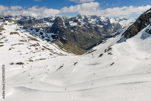 Obraz na płótnie Spring sunshine over Val Disere ski resort in the French Alps, snowboarders riding a snowboard cross course on soft snow, alpine scenery with mountains, blue sky in sunny spring, Tignes, France
