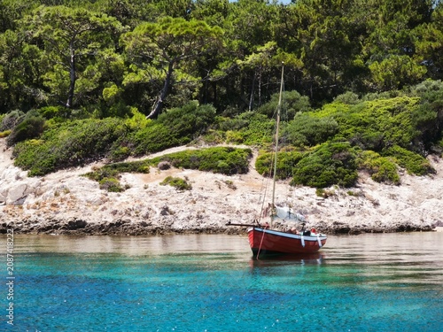 Red boat anchored in turquoise waters of Bademli Bay, Dikili, Izmir, Turkey